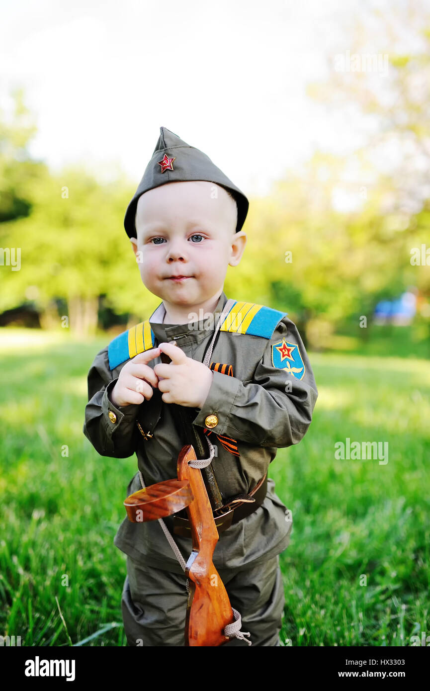 Un mignon petit enfant dans l'uniforme d'un soldat soviétique avec un ruban  de Saint-georges avec un pistolet en plastique sur le fond de la nature. Le  9 mai, le 23 février, defender,