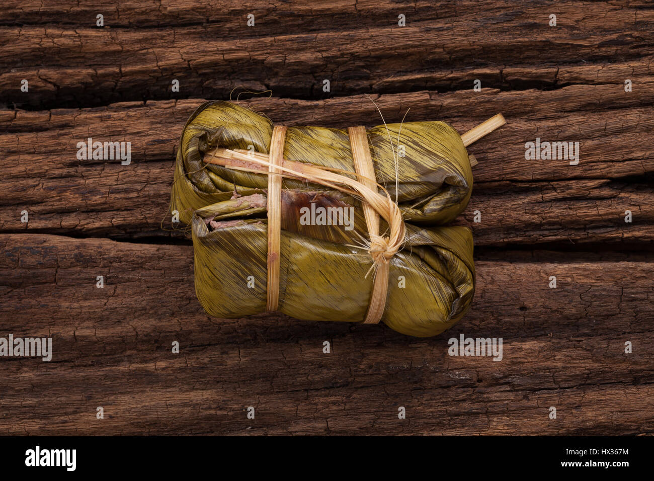 Khao Tom Mat - Thaï dessert - riz collant, banane et les haricots noirs enveloppés dans des feuilles de banane - still life close up sur fond de bois Banque D'Images