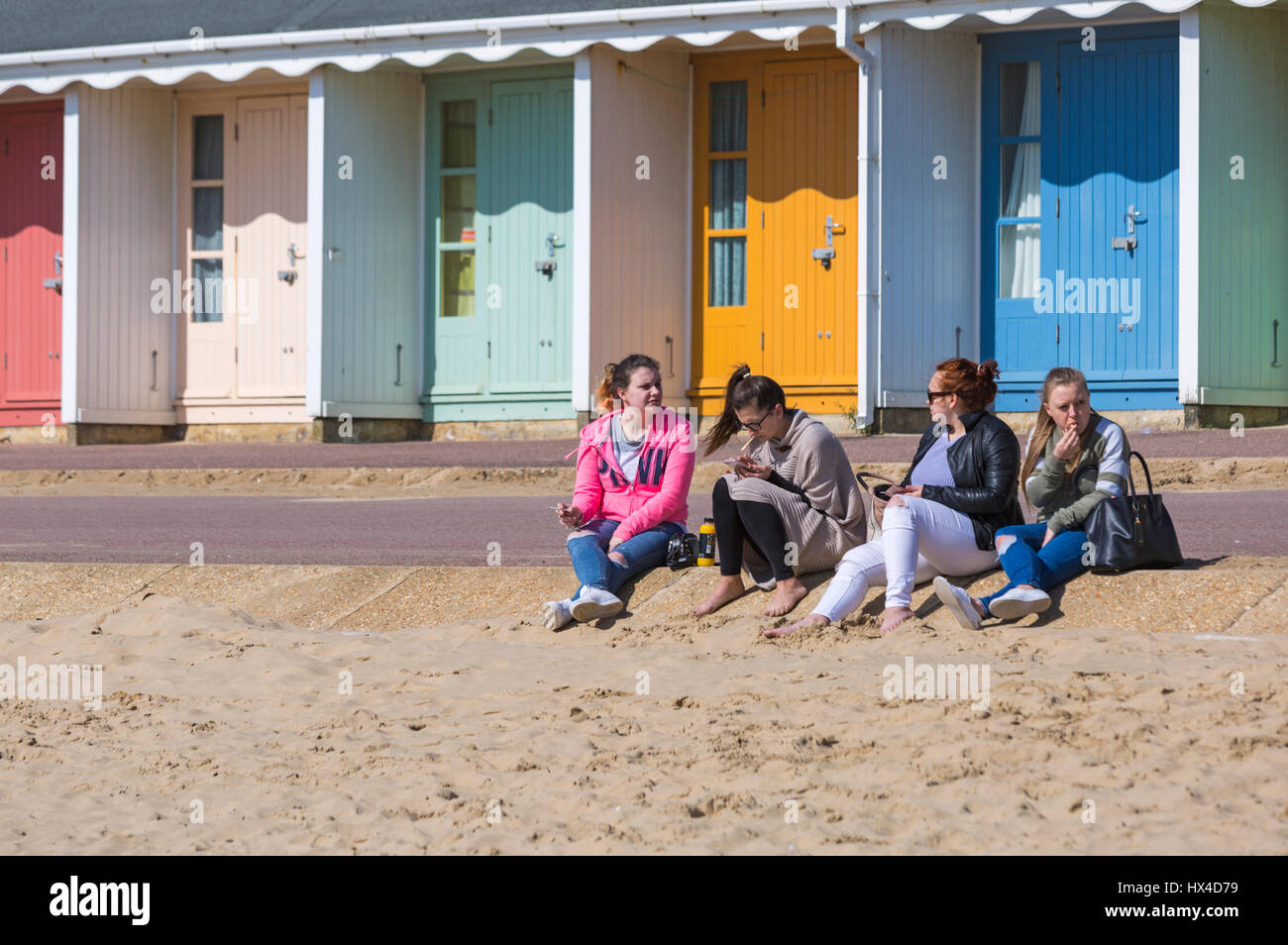 Bournemouth, Dorset, UK. Mar 25, 2017. Météo France : belle chaude journée ensoleillée comme visiteurs chef de la mer à profiter du soleil sur les plages de Bournemouth. Quatre jeunes femmes assis sur le sable en face de la promenade de cabines colorées à la plage de Bournemouth. Credit : Carolyn Jenkins/Alamy Live News Banque D'Images