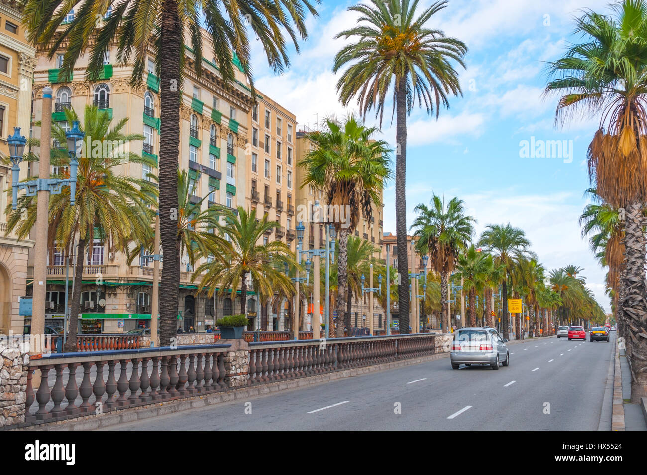 Voitures dans la rue, la fin de l'après-midi à Barcelone. Rue bordée de palmiers avec vacances & condo buildings aux gens de se rencontrer dans un café à l'autre côté de la rue. Banque D'Images