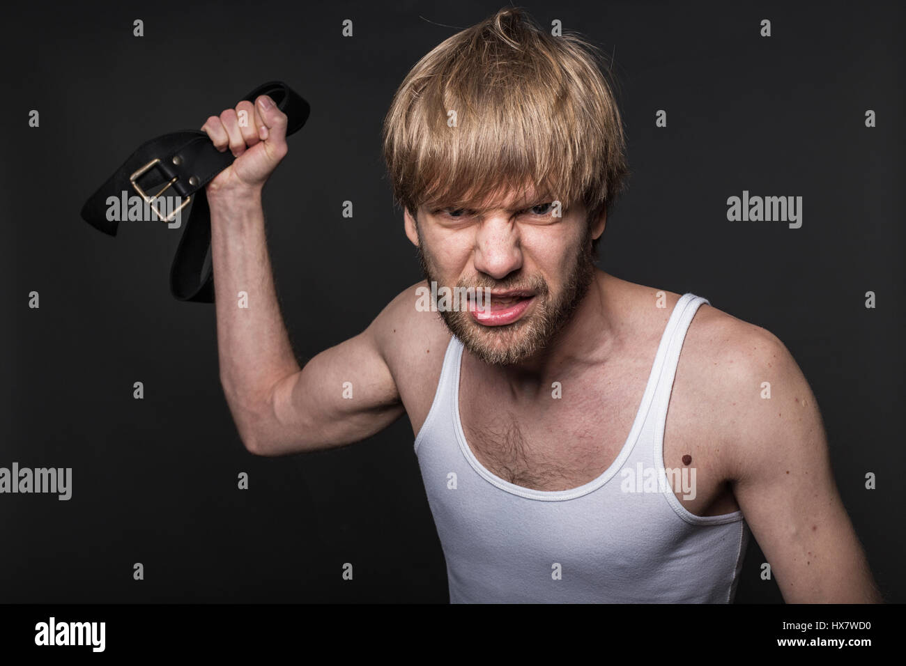 Homme en colère menace avec ceinture. Concept : La violence contre les femmes. Studio portrait sur fond noir Banque D'Images