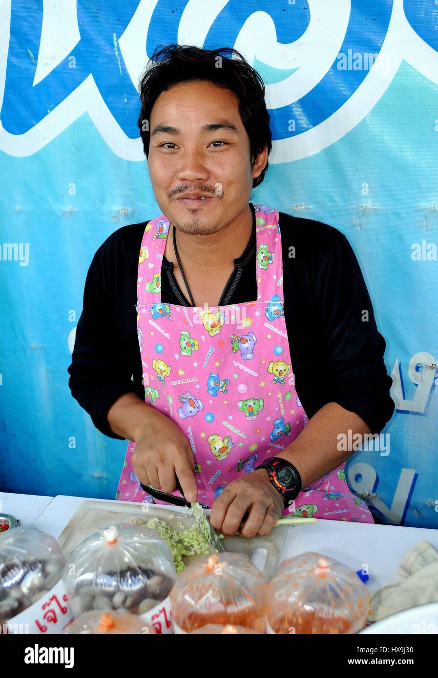 Amphawa, Thaïlande - 17 décembre 2010 : Smiling man chopping les oignons verts à son stand le long du quai du marché flottant d'Amphawa Banque D'Images