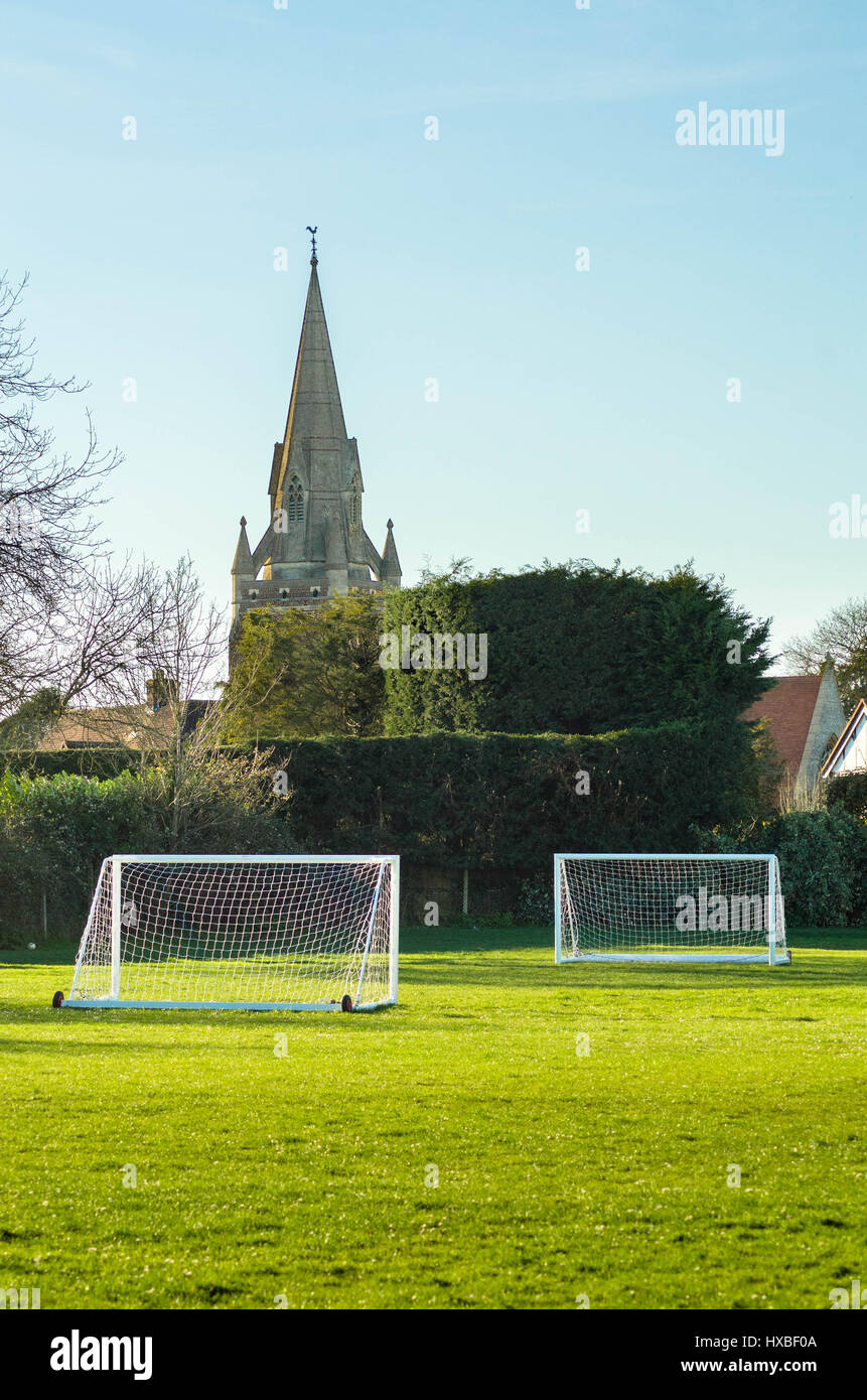 La recherche à travers un terrain de jeu avec des buts de football à l'avant-plan et une église avec un clocher à l'arrière-plan. Banque D'Images