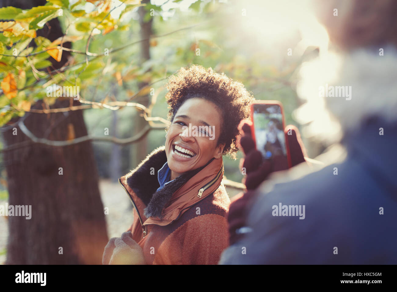 Smiling woman posing for boyfriend with camera phone in sunny autumn woods Banque D'Images