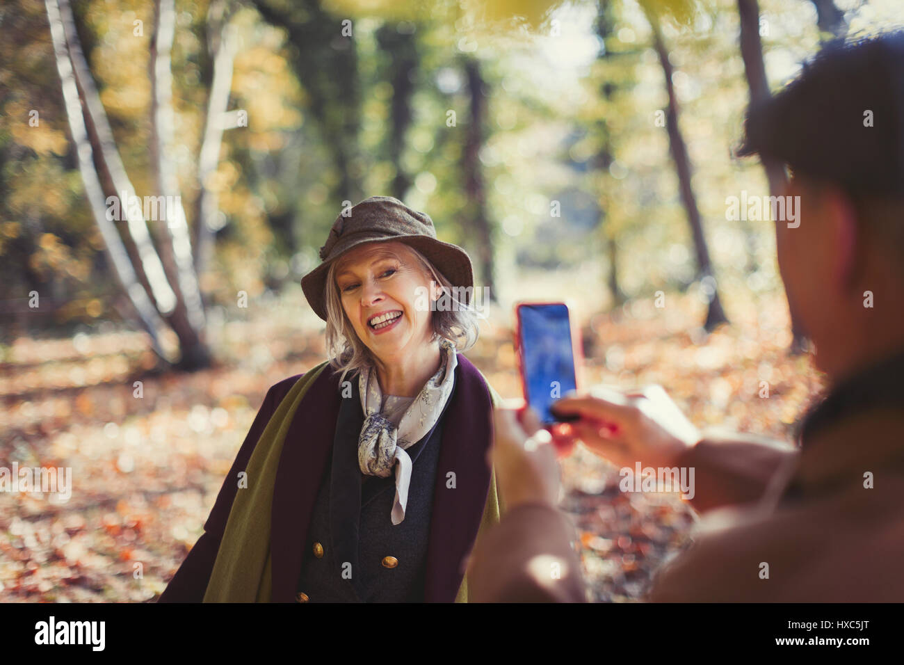 Senior woman ludique photographiée par mari avec camera phone in autumn park Banque D'Images