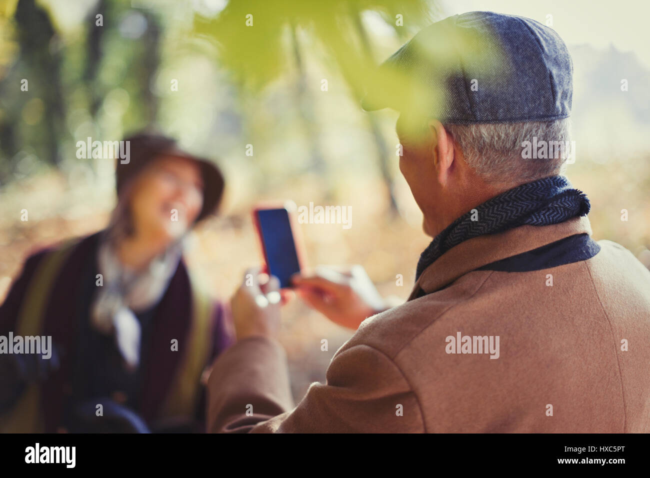 Senior man with camera phone photographing wife in park Banque D'Images