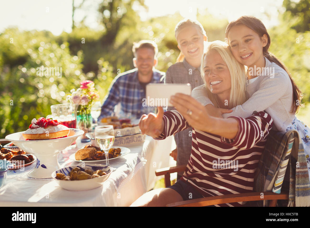 La mère et les filles en tenant avec selfies camera phone at garden party table patio Banque D'Images