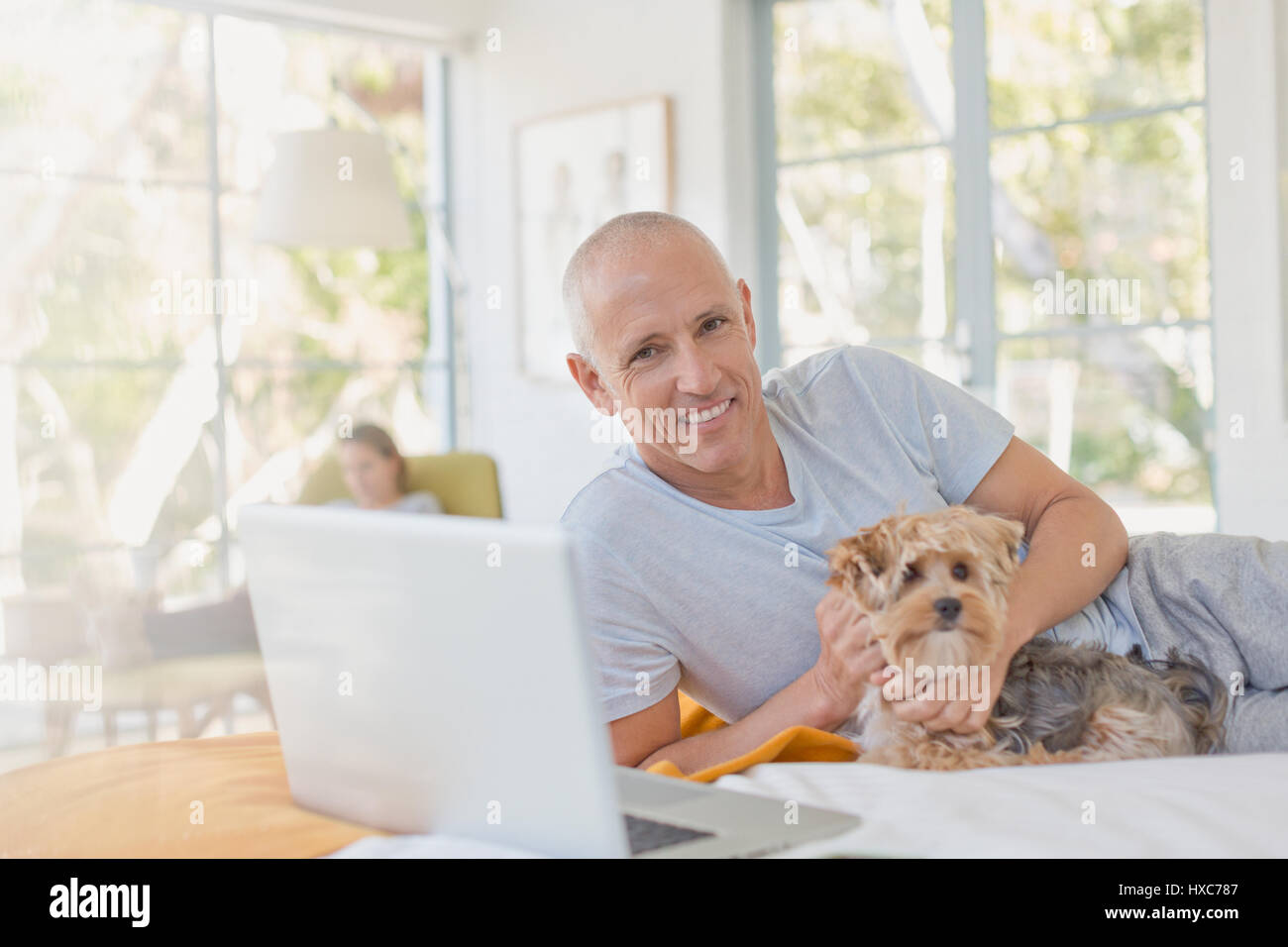 Portrait smiling man petting dog on bed at laptop Banque D'Images