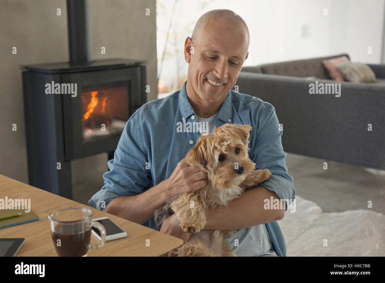Smiling man petting dog in front of poêle à bois cheminée Banque D'Images