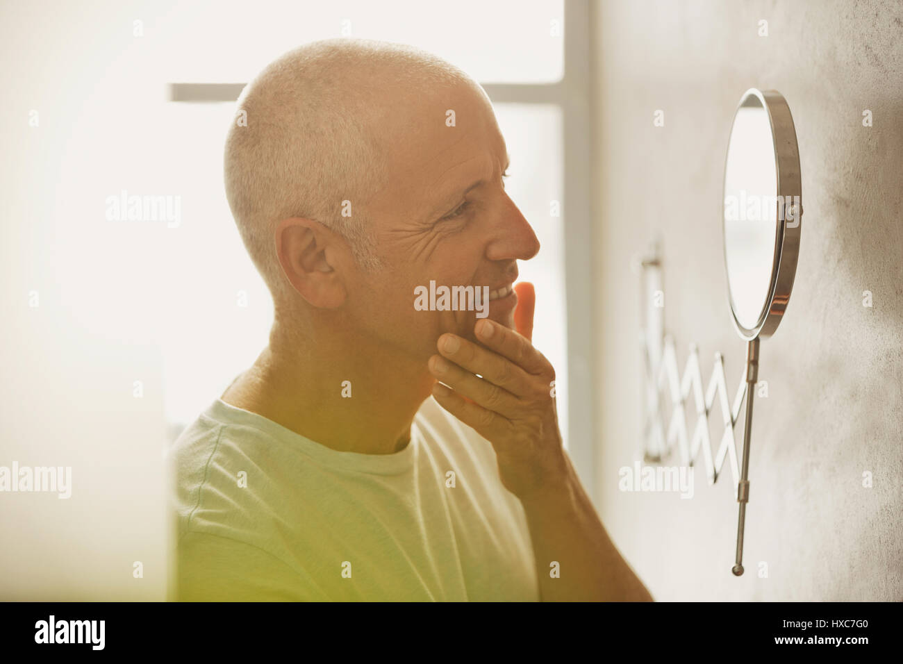 L'homme à la peau mature au grossissement en miroir dans salle de bains Banque D'Images