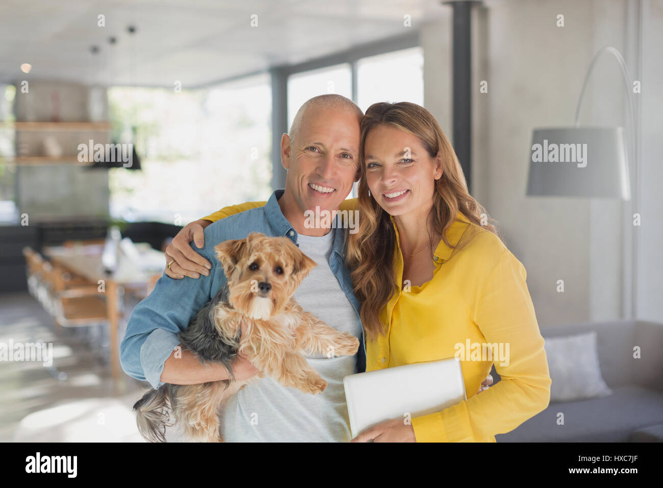 Portrait of smiling mature couple hugging dog in living room Banque D'Images