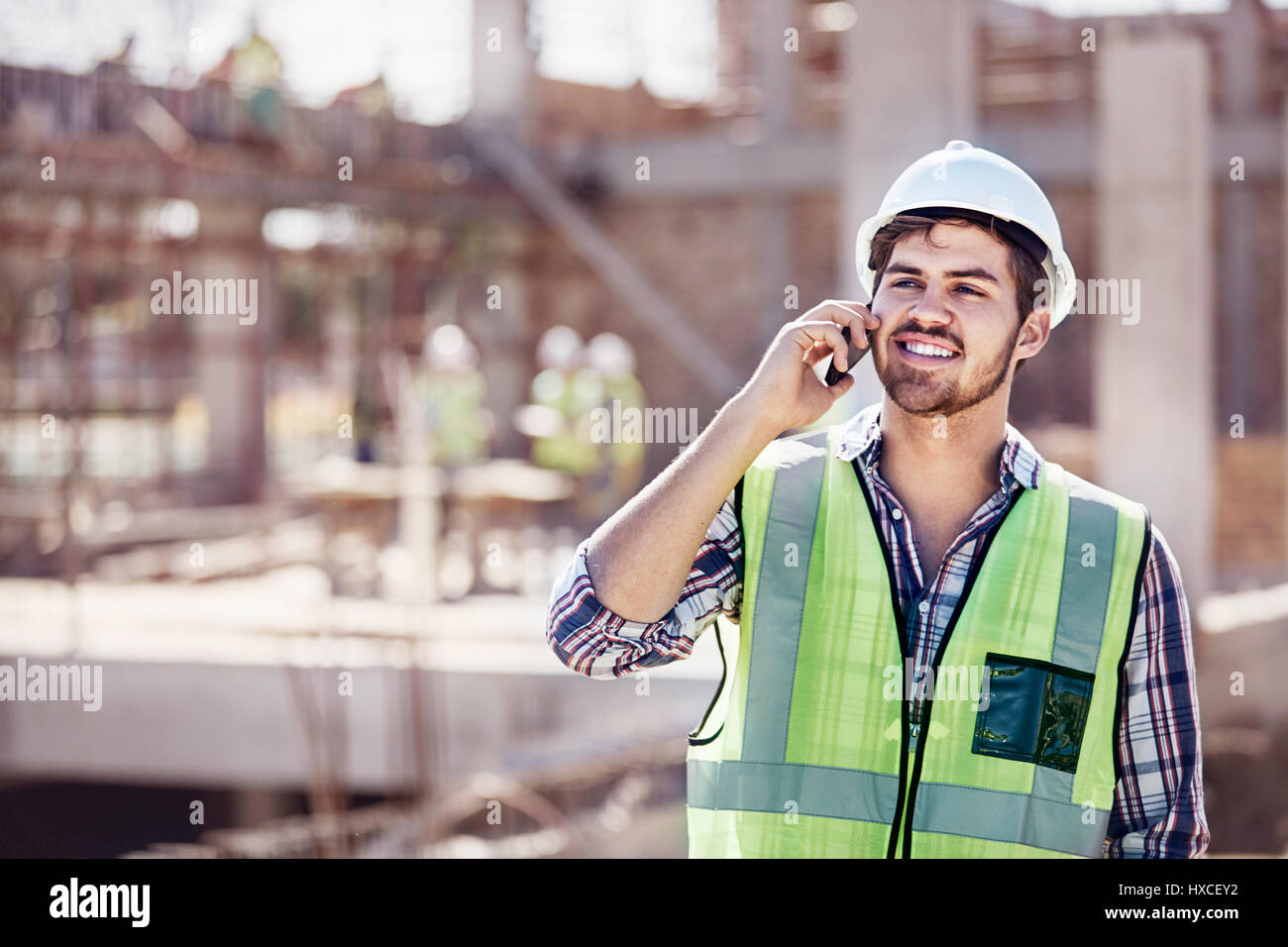 Construction Worker talking on cell phone at construction site ensoleillé Banque D'Images