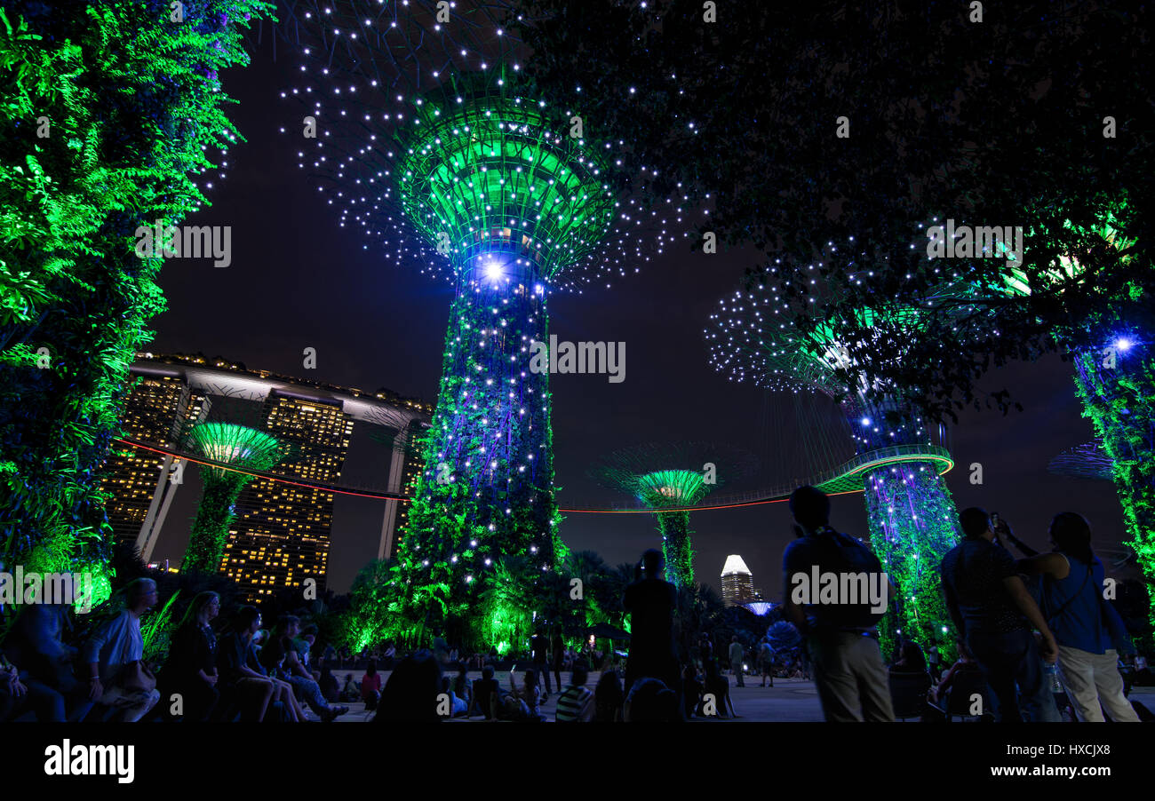 Temps de nuit vers le haut des arbres et lumière dans les jardins de la baie avec des personnes en premier plan et Marina Bay Sands Hotel. Banque D'Images