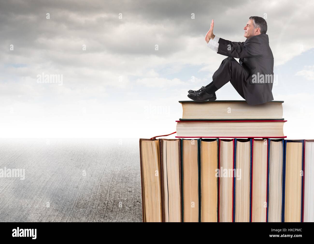 Digital composite de l'homme assis sur les livres empilés par ciel nuageux gris Banque D'Images