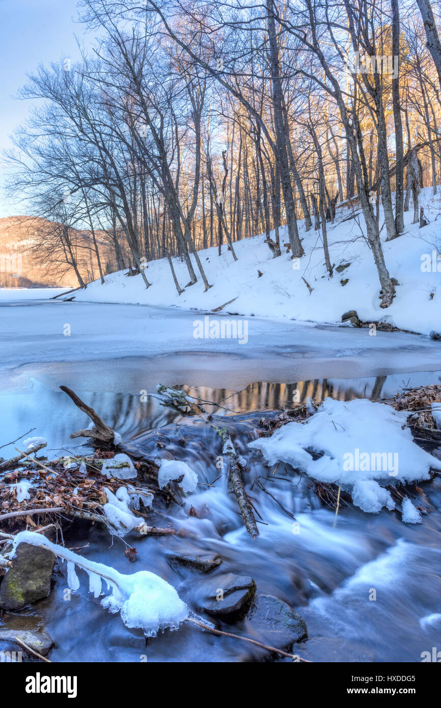 Réflexions et ondulations dans l'eau qui s'écoule du Grand Étang partiellement gelé dans les Catskills Mountains of New York. Banque D'Images