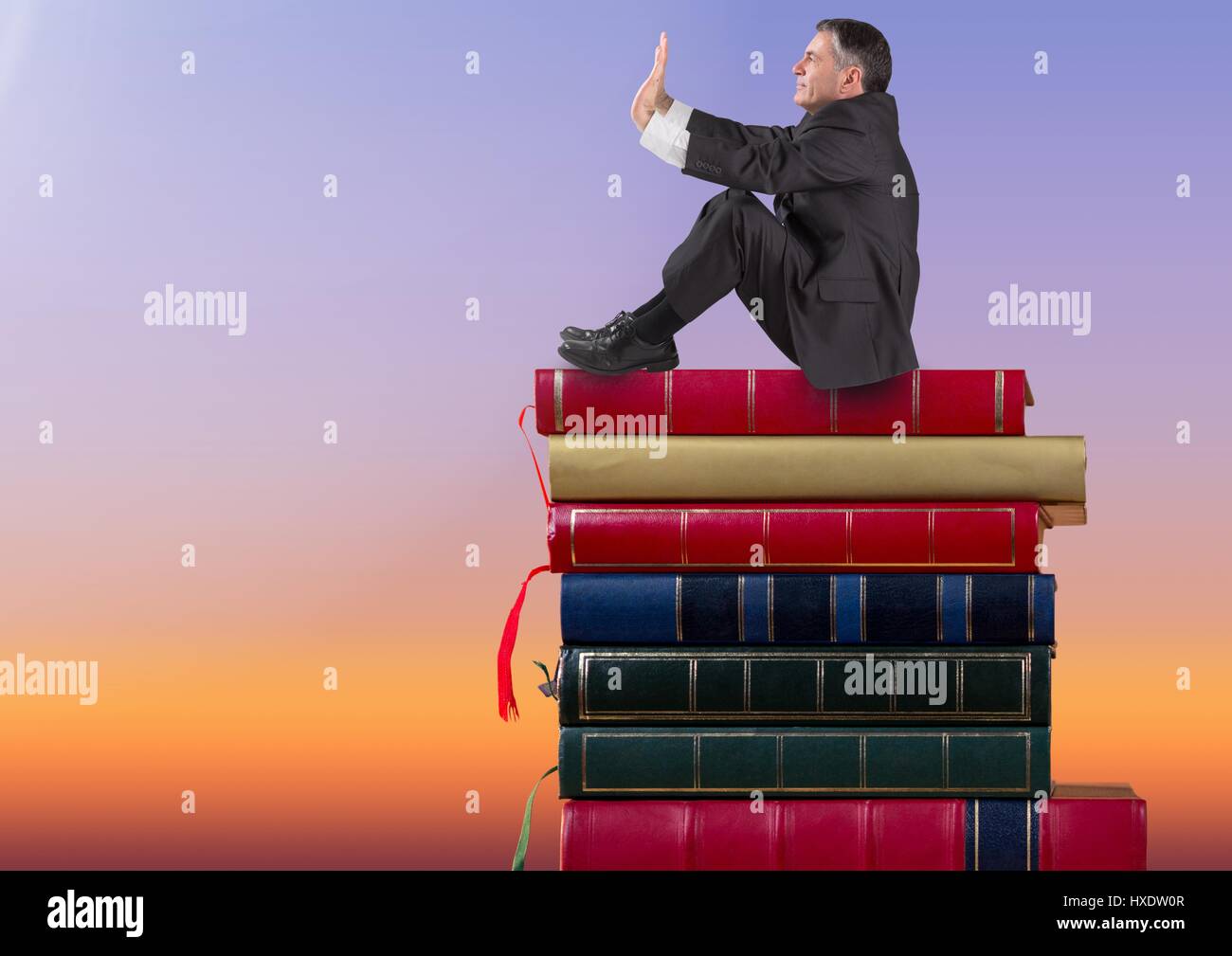 Digital composite of Businessman sitting on Books empilées par ciel crépusculaire Banque D'Images