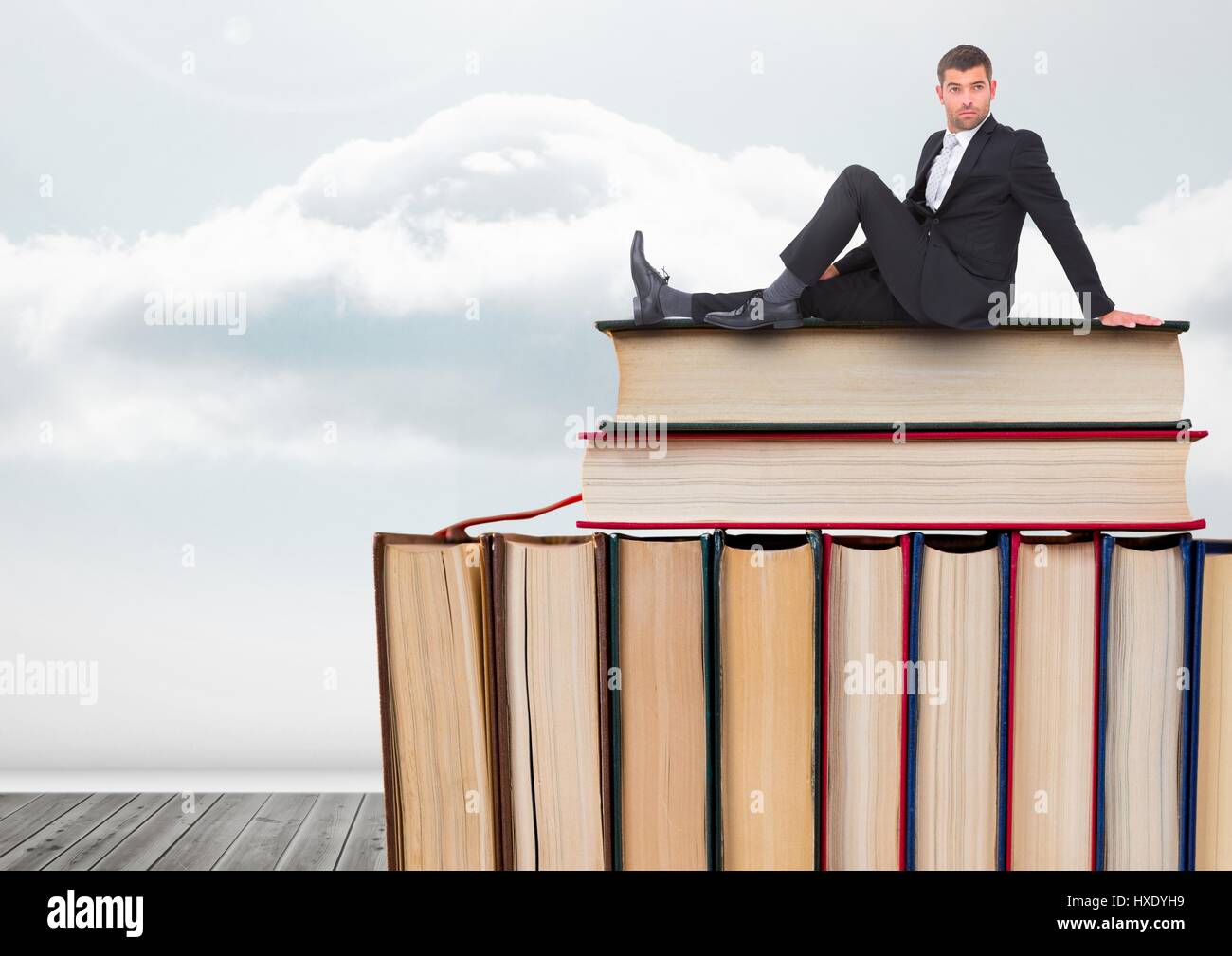 Digital composite de l'homme assis sur les livres empilés par ciel nuageux Banque D'Images