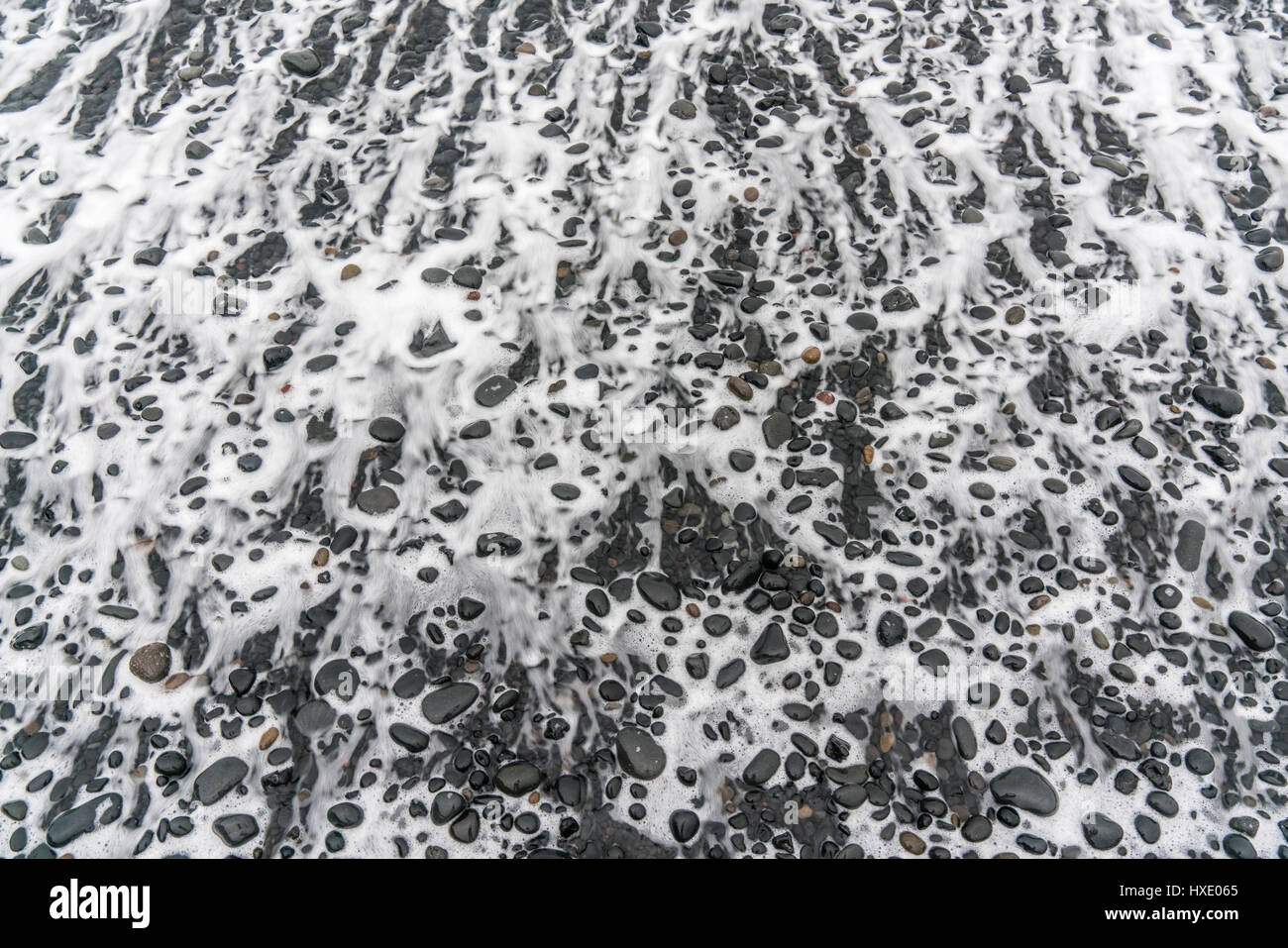 Les vagues de l'océan s'éloignent le long du surf sur une plage de sable noir en Islande Banque D'Images