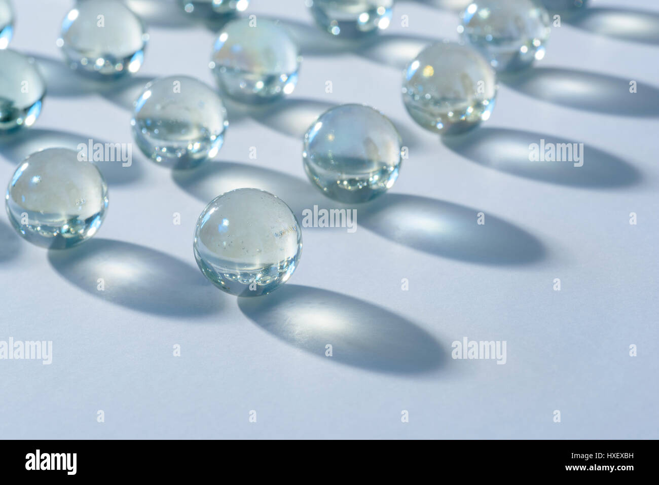 Billes de verre clair sur une surface blanche baignée d'une lumière bleue Banque D'Images