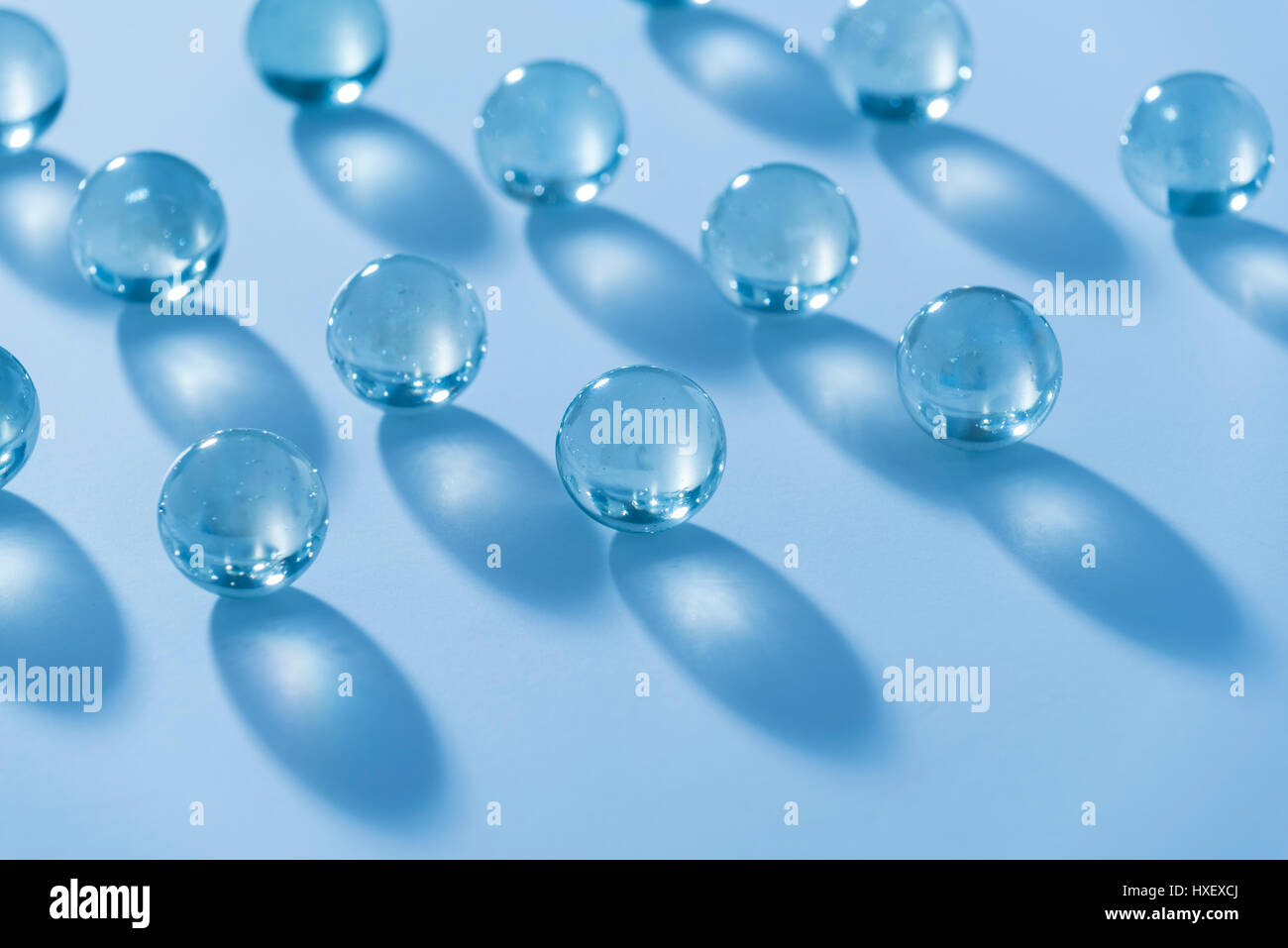 Billes de verre clair sur une surface blanche baignée d'une lumière bleue Banque D'Images