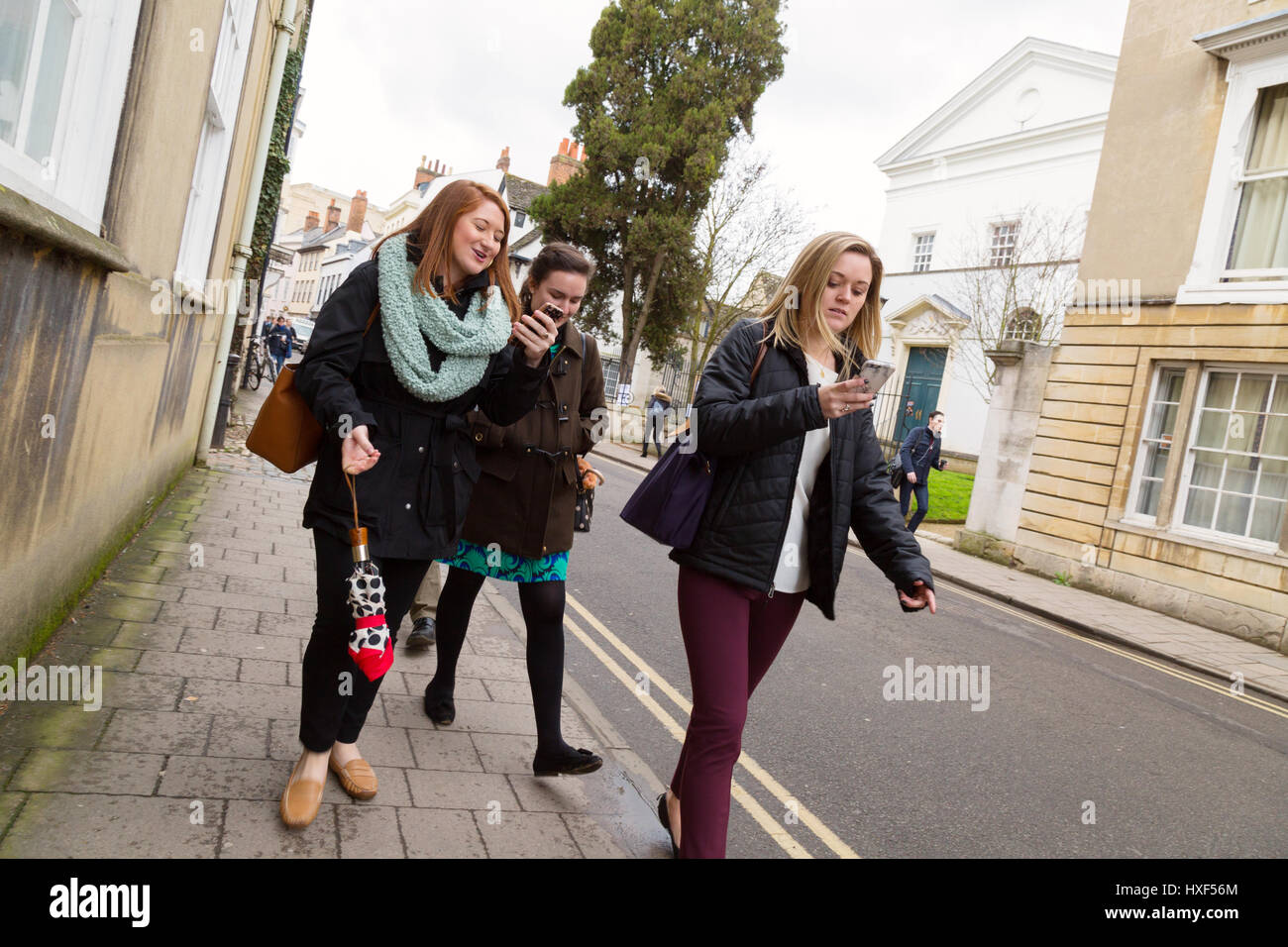 Trois jeunes femmes marchant dans la rue à l'aide de leur téléphone mobile, Oxford UK Banque D'Images