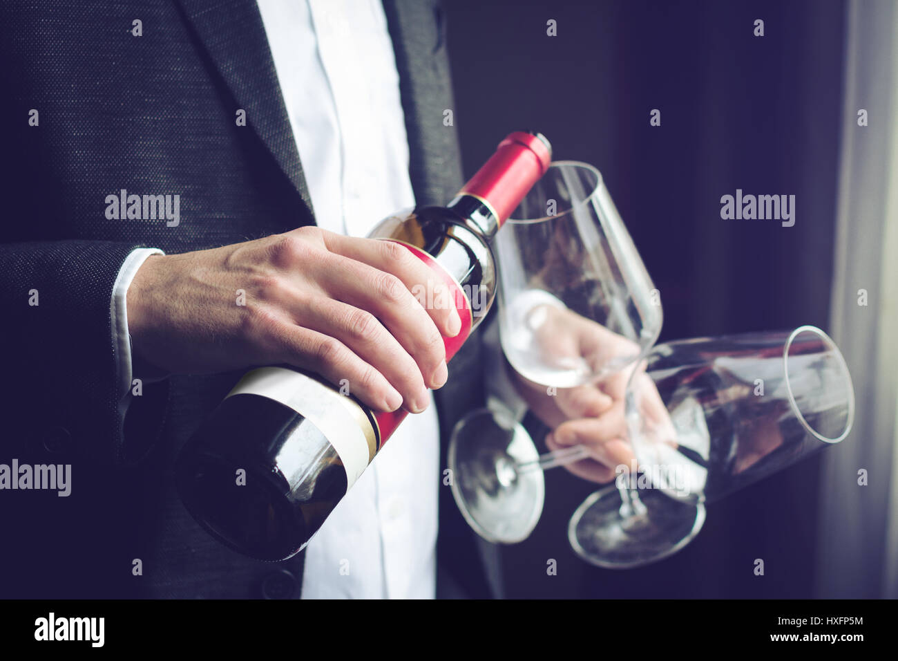 Close up of Horizontal Caucasian man en costume noir et chemise blanche verser le vin rouge dans un grand verre dans un bar à l'éclairage naturel Banque D'Images