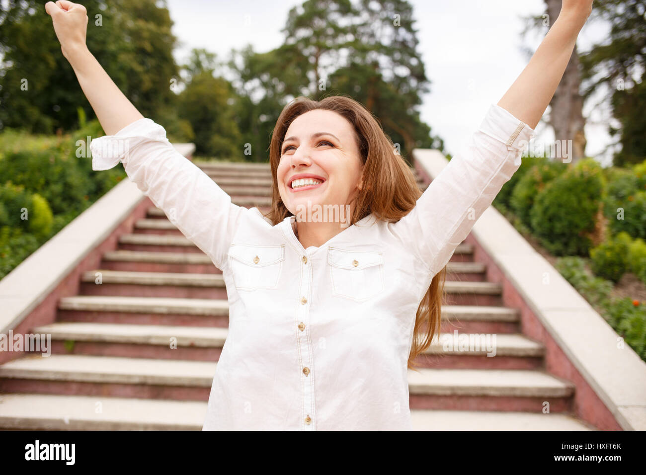 Femme heureuse avec main levée debout près des escaliers en parc. Fille hispanique à la hâte Banque D'Images