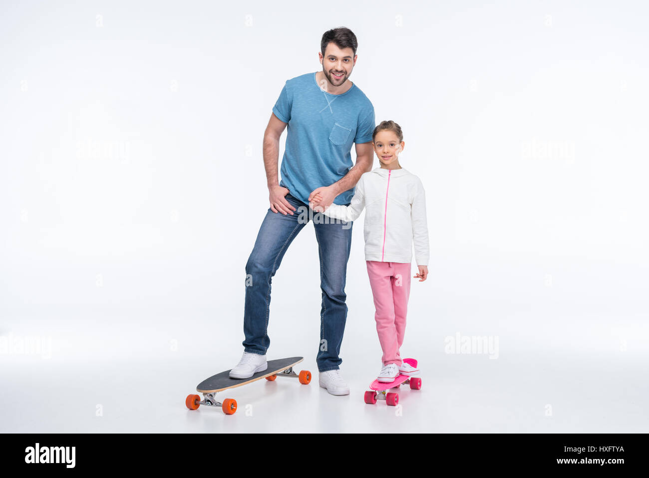 Smiling father and daughter standing with skateboards on white Banque D'Images