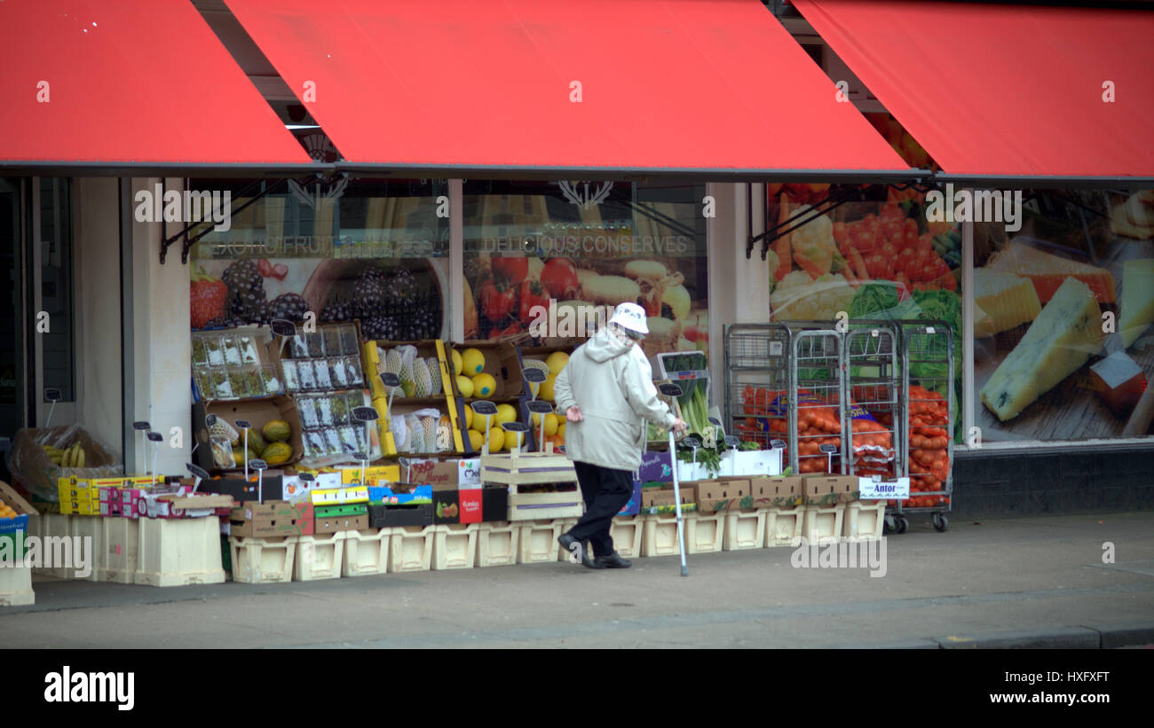 Ol'femme chinoise avec mal au dos et bâton de marche à l'extérieur de magasin de fruits Banque D'Images