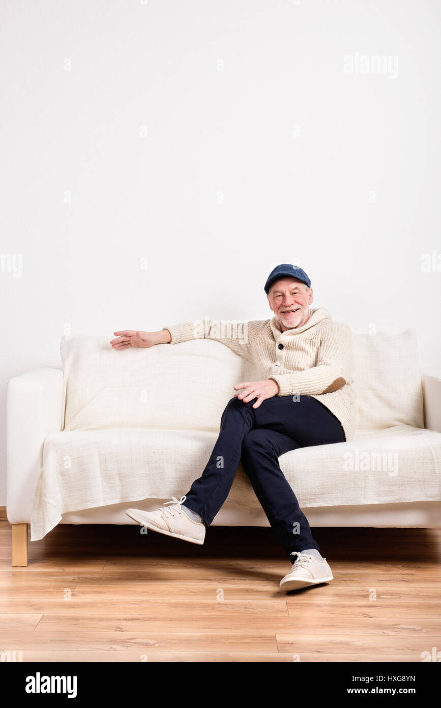 Handsome man pull beige en souriant, assis sur un canapé, les jambes croisées. Studio shot contre le mur blanc. Banque D'Images