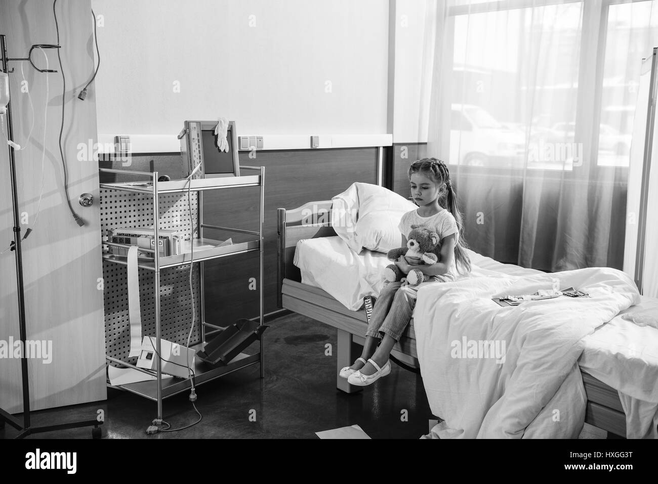 Photo en noir et blanc de upset girl avec ours assis sur lit d'hôpital Banque D'Images