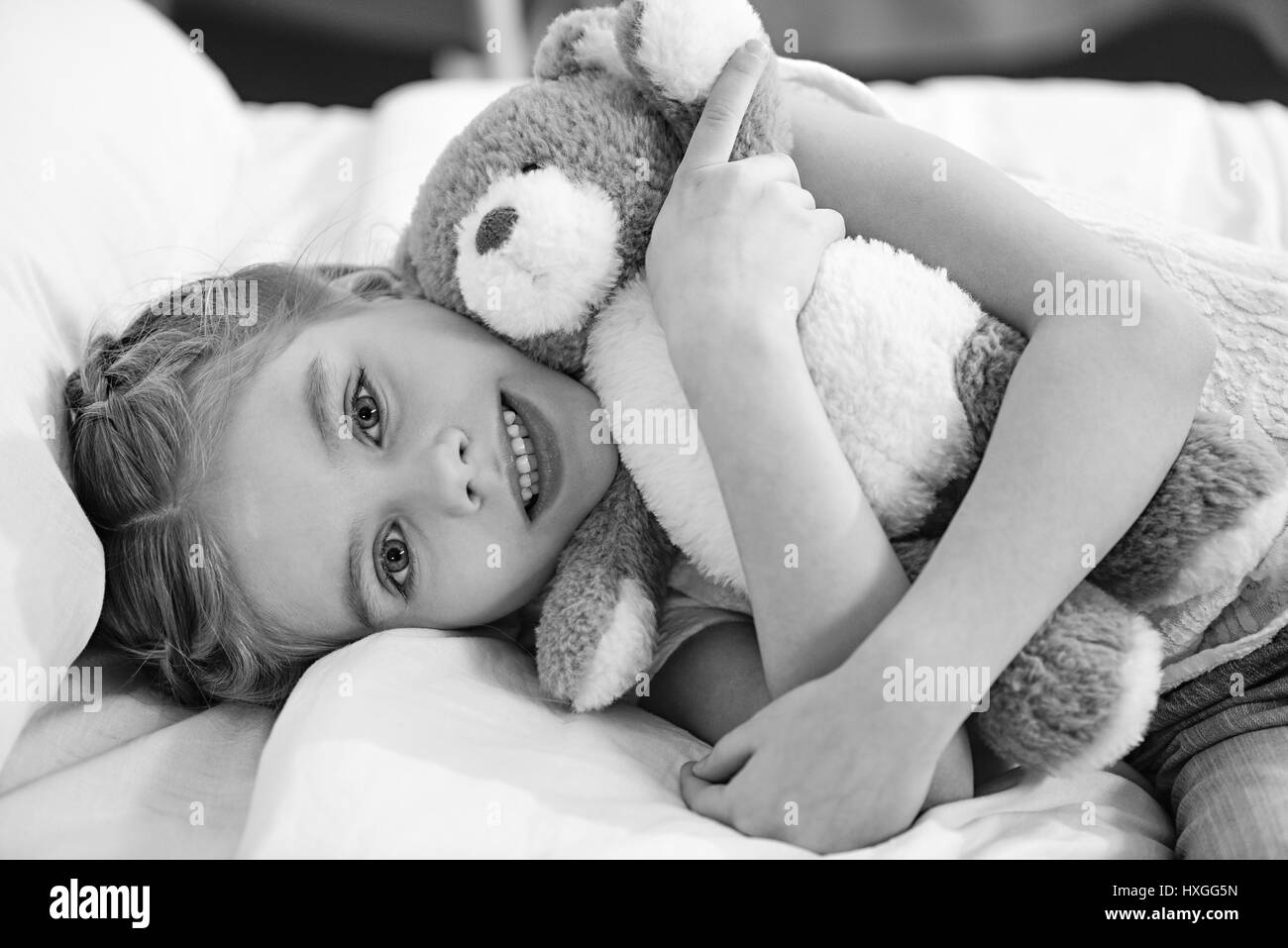 Smiling little girl avec ours couché dans lit d'hôpital, photo en noir et blanc Banque D'Images