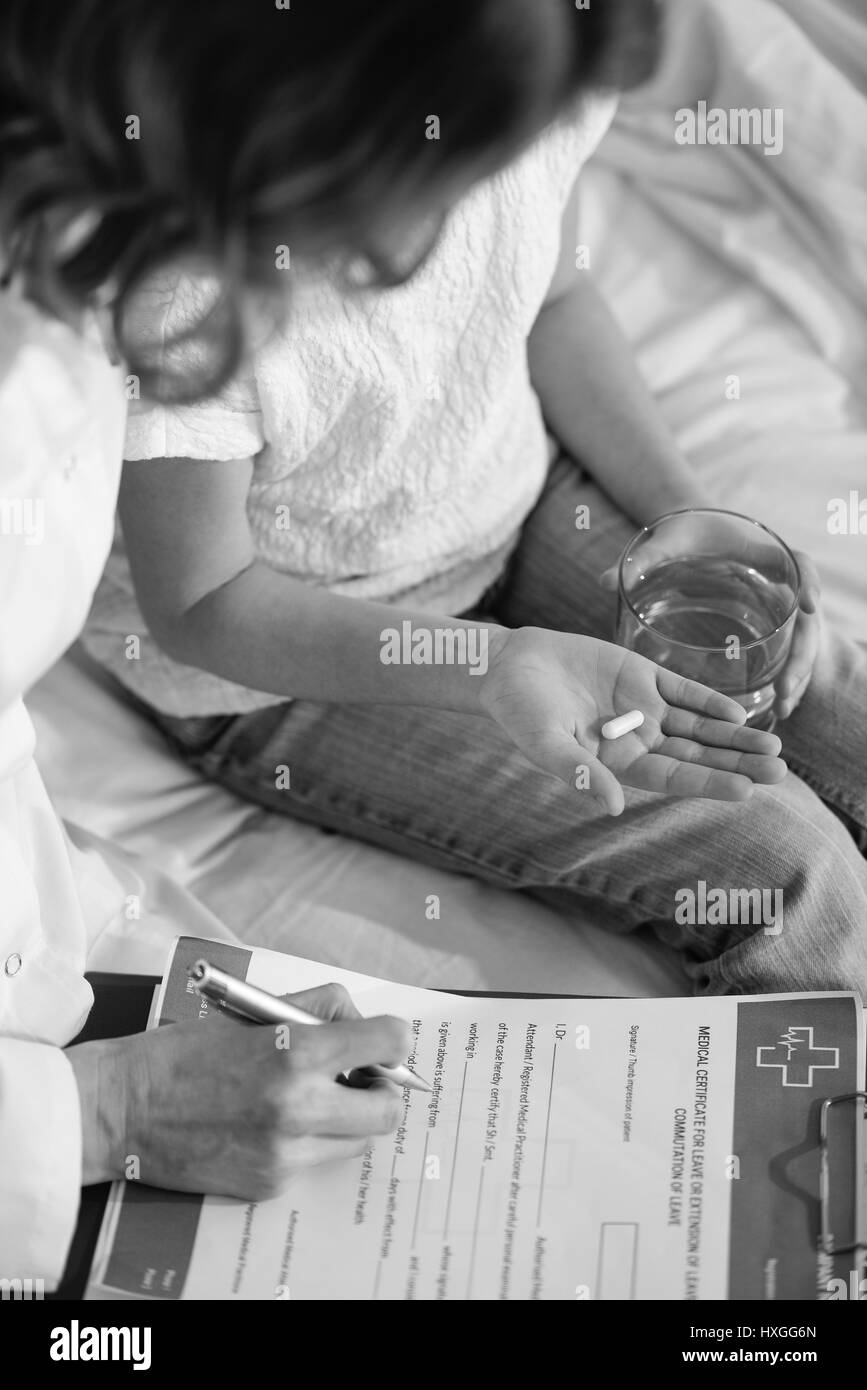 Vue partielle de médecin avec presse-papiers et little girl holding pill assis sur le lit, photo en noir et blanc Banque D'Images