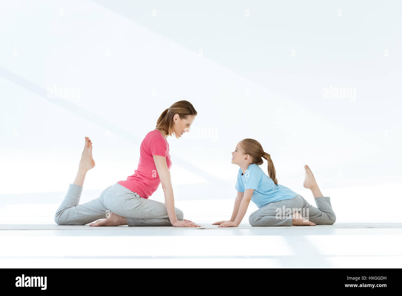 Smiling mother and daughter pratiquer yoga pigeon sur des nattes et à la recherche à l'autre Banque D'Images