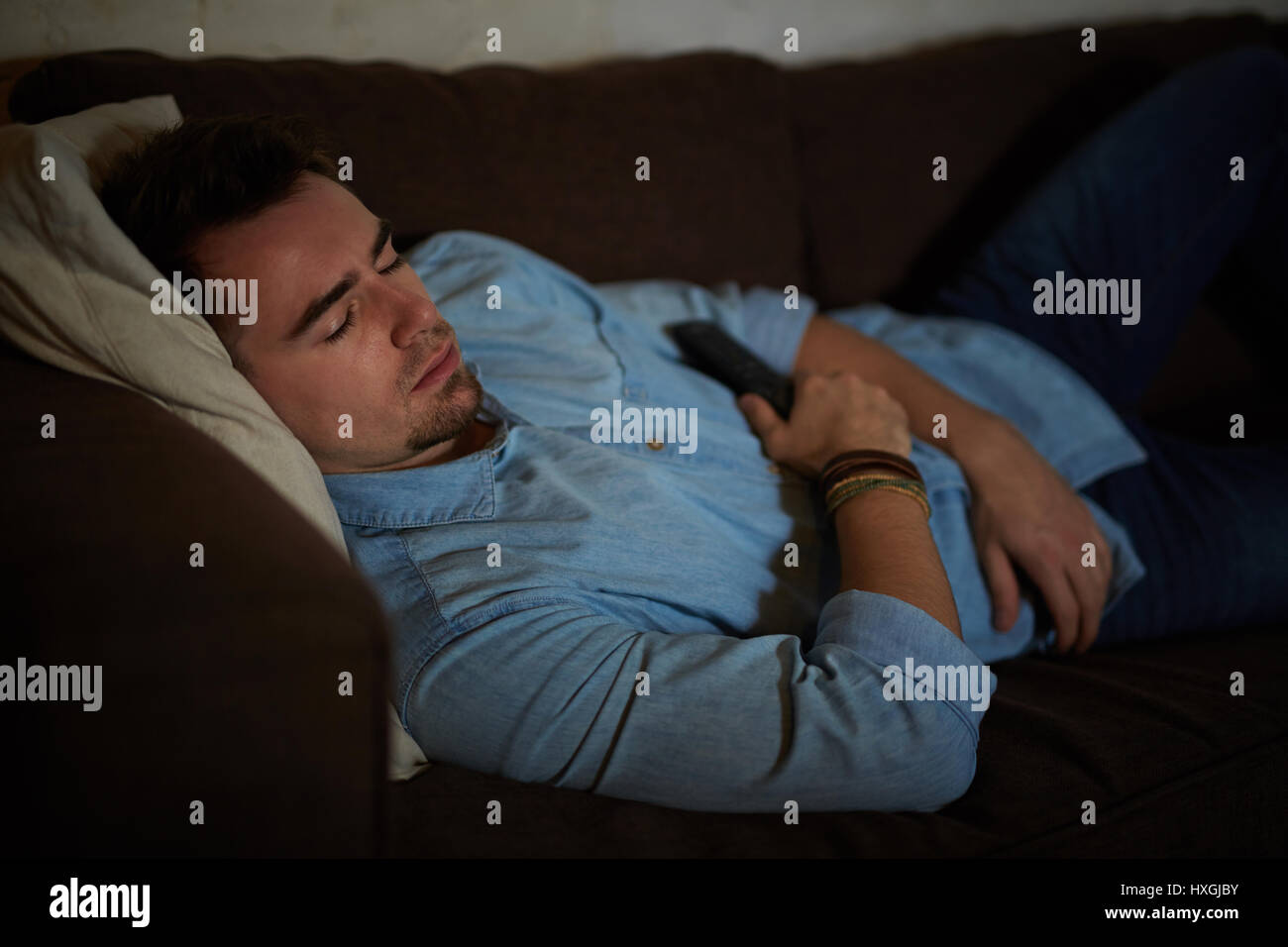 Portrait de jeune homme s'endormir sur le canapé dans la pièce sombre , holding remote contrôleur tout en regardant la télévision tard dans la nuit Banque D'Images