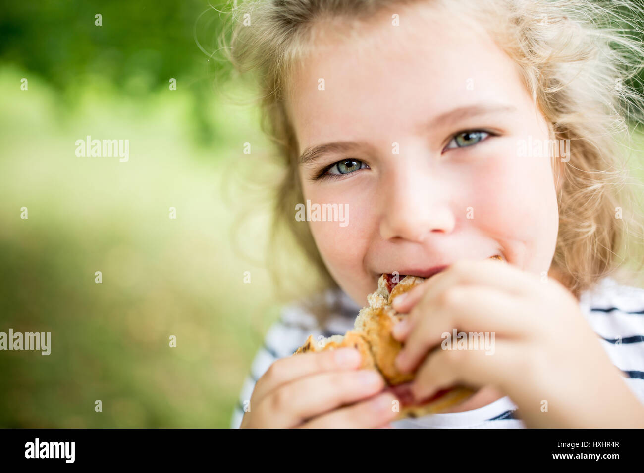 Girl eating snack-bun au parc en été hors de la faim Banque D'Images