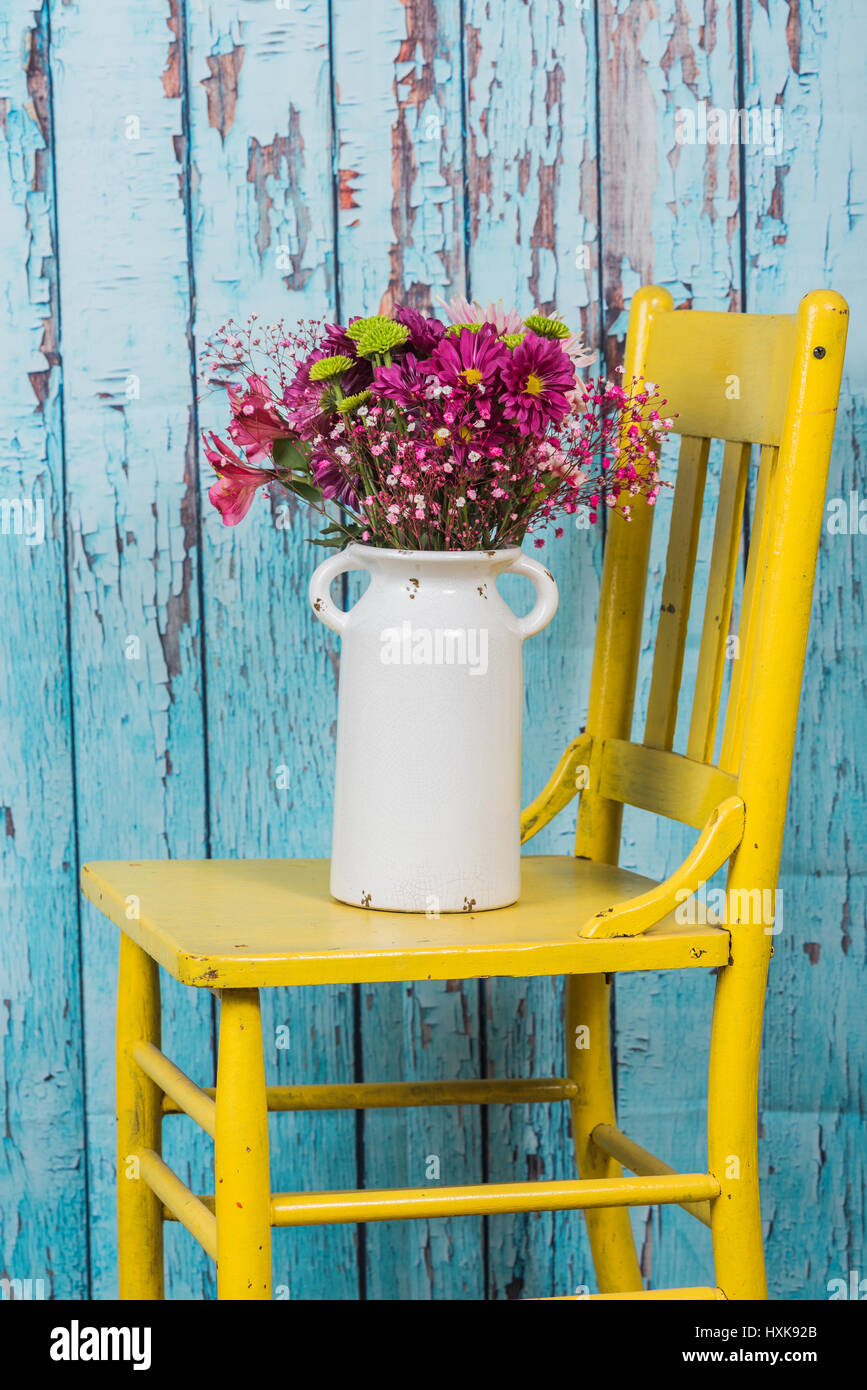 Bouquet de fleurs dans vase vintage assis sur chaise jaune Banque D'Images