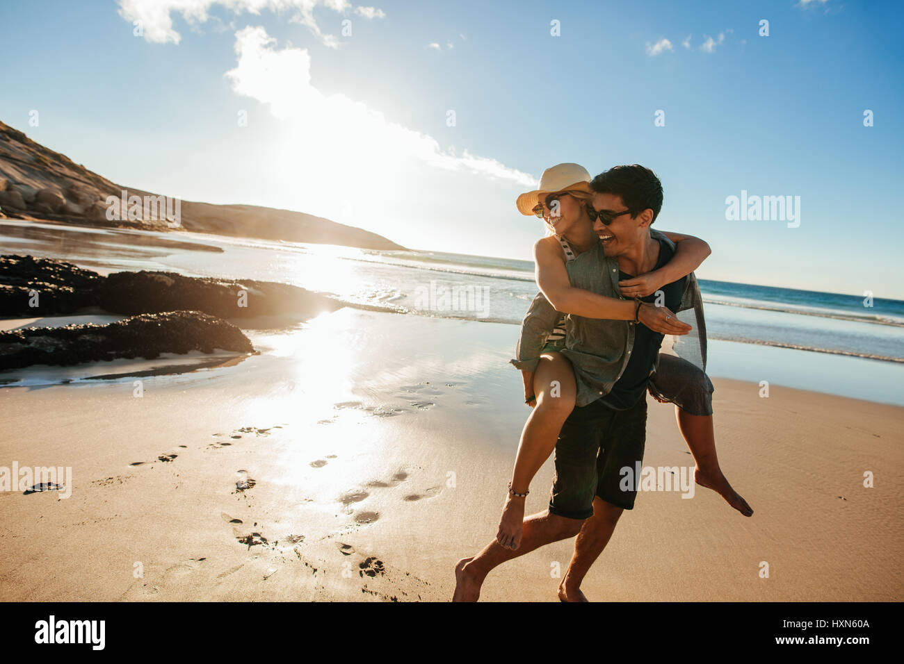 Jeune couple romantique appréciant des vacances d'été. Beau jeune homme donnant à piggyback ride pour petite amie sur la plage. Banque D'Images
