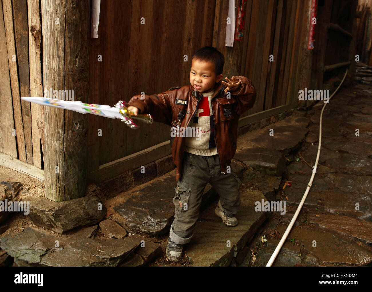 La province de Guangxi, Chine - le 4 avril : 6 ans, jouer avec l'épée en plastique près de maison en bois dans village Changan, le 4 avril 2010. Village i Banque D'Images