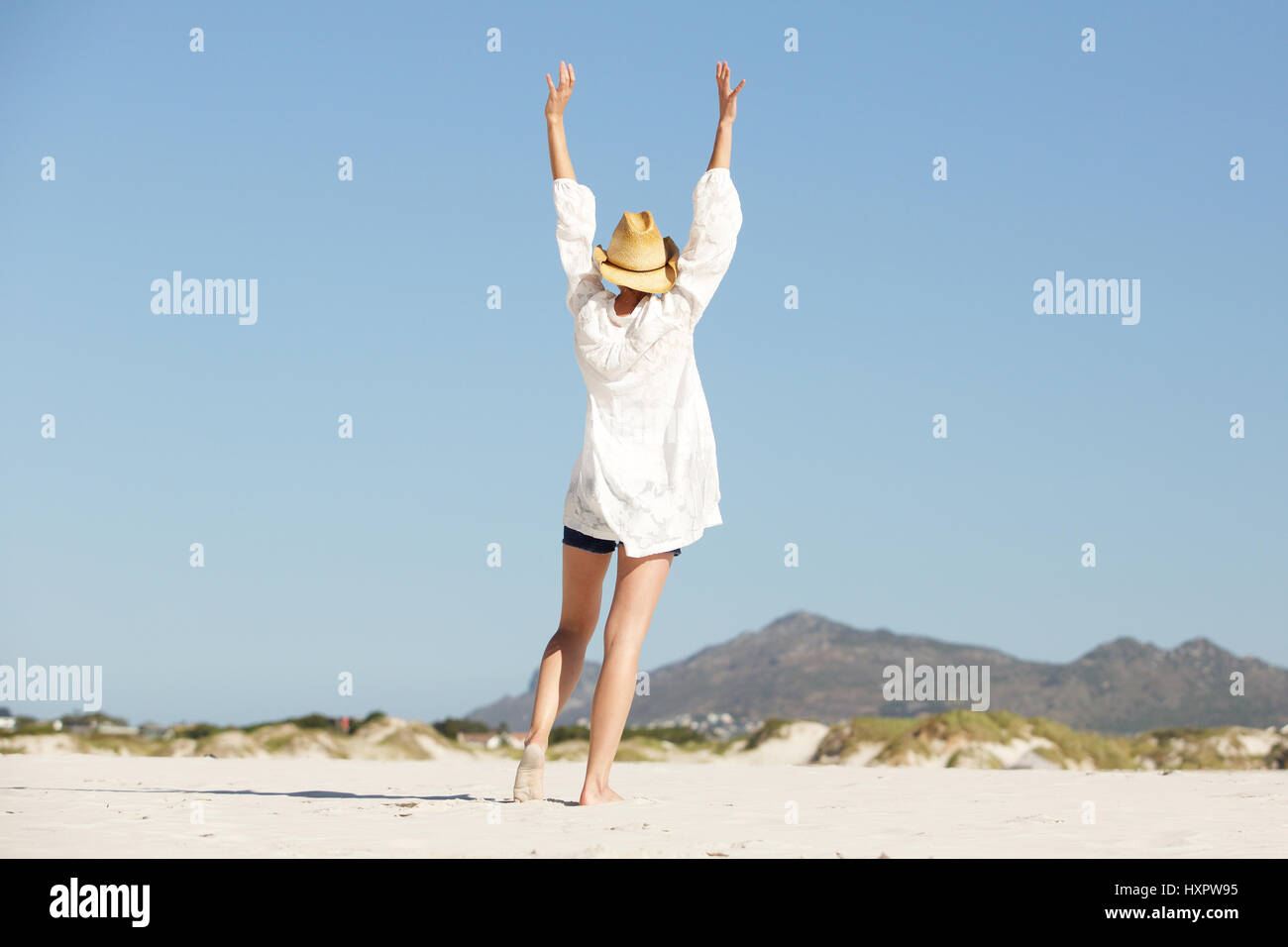 Portrait de jeune femme avec bras levés la marche sur la plage de derrière Banque D'Images