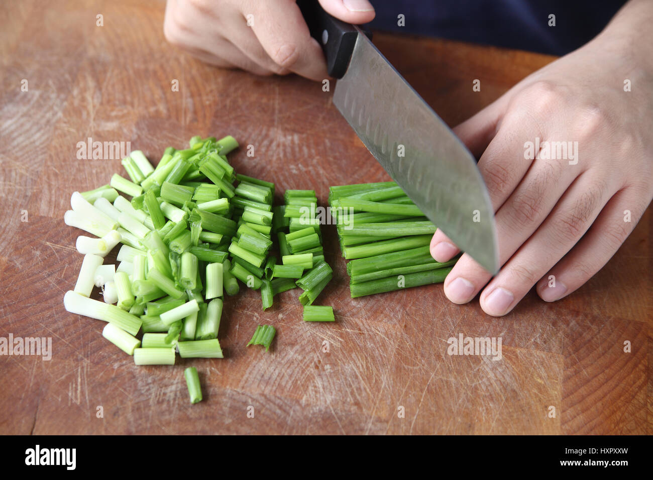 Un homme utilise un couteau de chef pour hacher les échalotes sur une planche à découper Banque D'Images