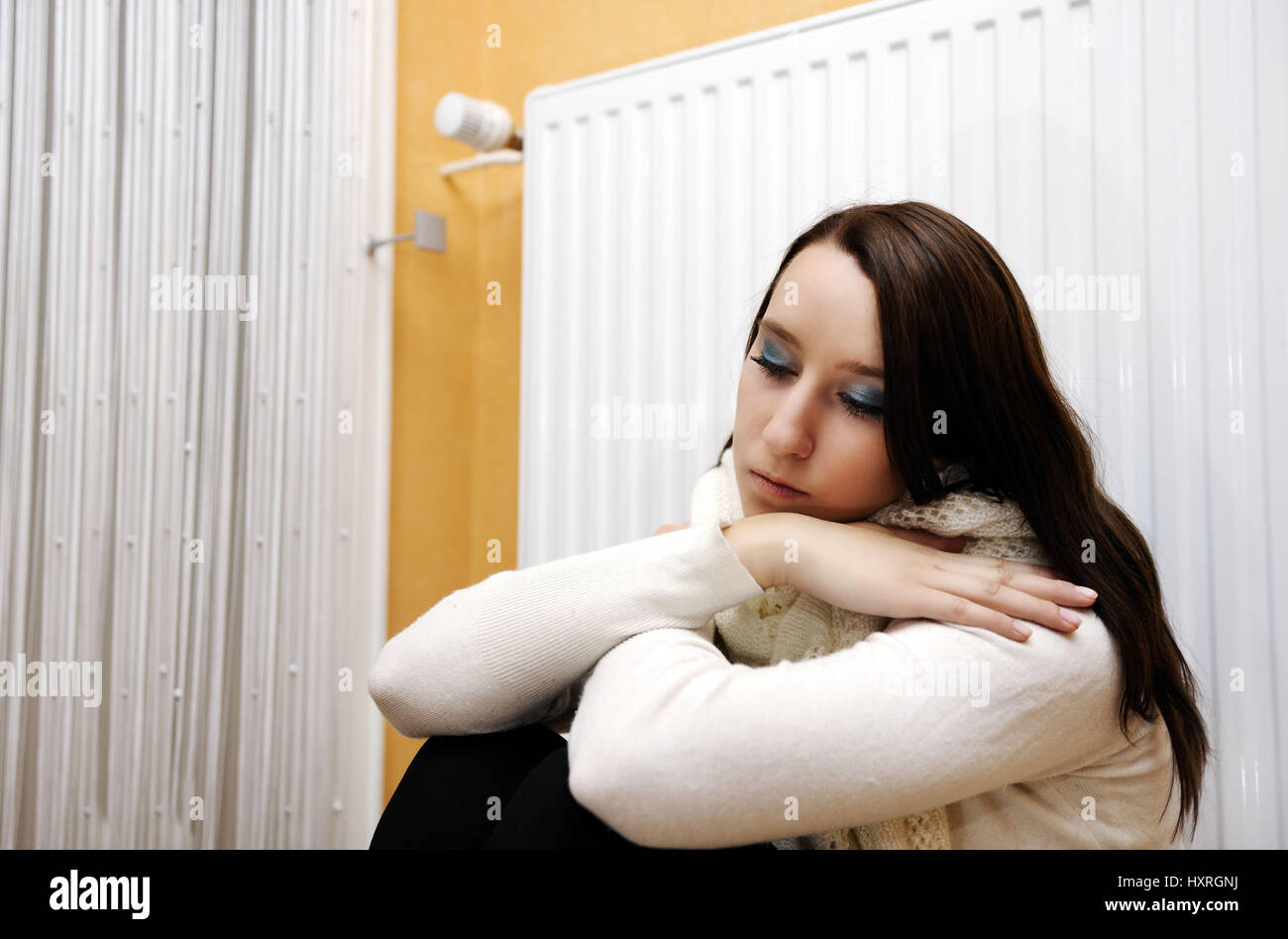 Jeune femme assise gel avant le chauffage, les coûts de chauffage, Junge Frau sitzt vor der Heizung, frierend Heizkosten Banque D'Images