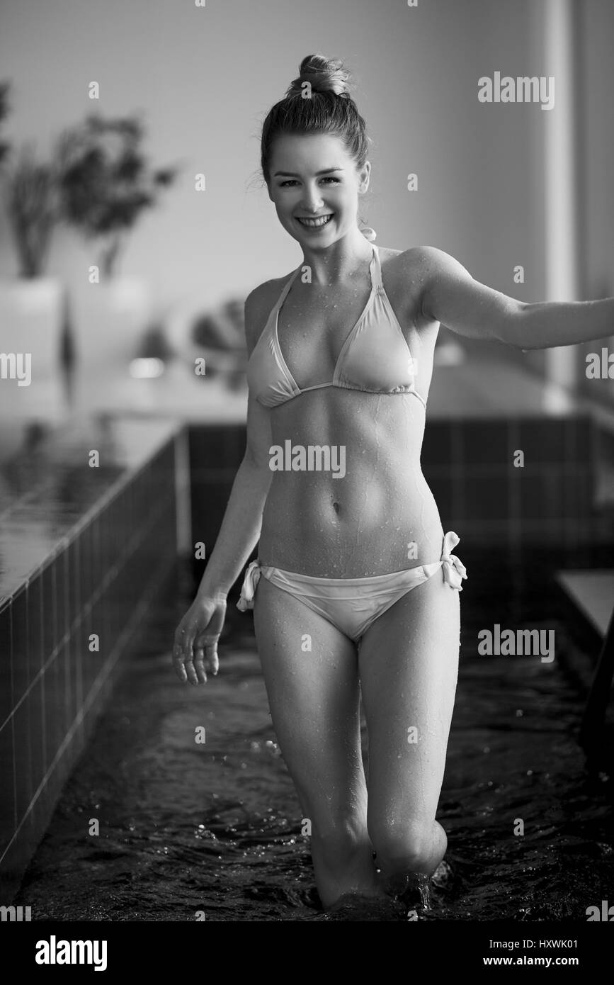 Beau young woman standing in swimming pool en jaune maillot de bain deux pièces, à l'écart et souriant Banque D'Images