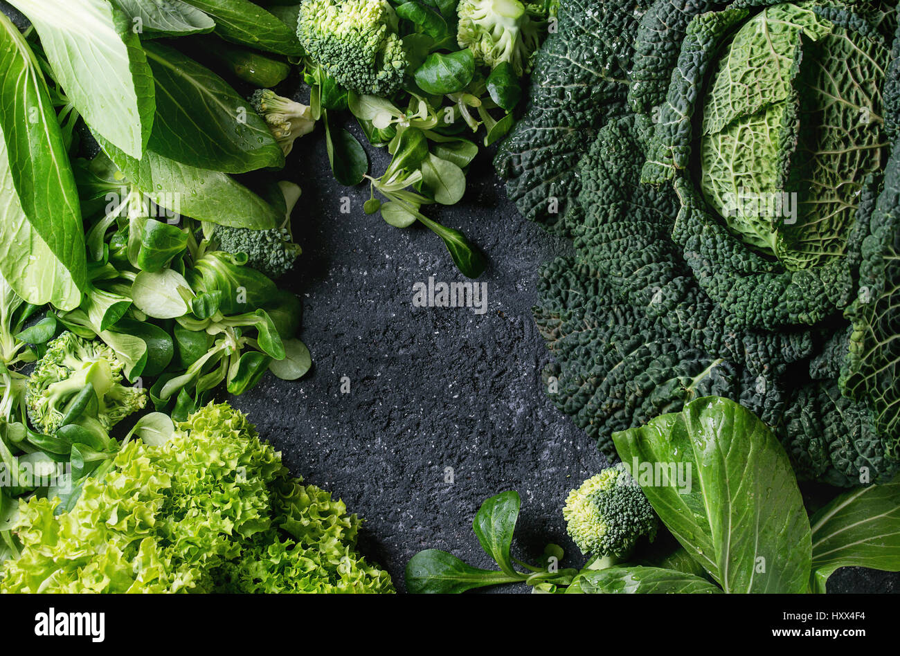 Variété de légumes verts crus des salades, la laitue, le bok choy, maïs, brocoli, chou de Milan en tant que cadre sur pierre noire texture background. Vue de dessus, de l'espace Banque D'Images