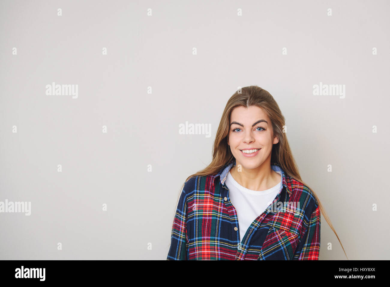 Studio portrait of happy young woman posing chemise à carreaux contre mur. Banque D'Images