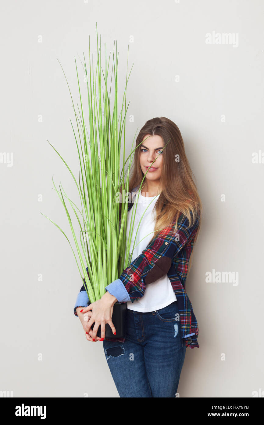 Studio portrait of beautiful young woman holding big green plant debout contre le mur. Banque D'Images