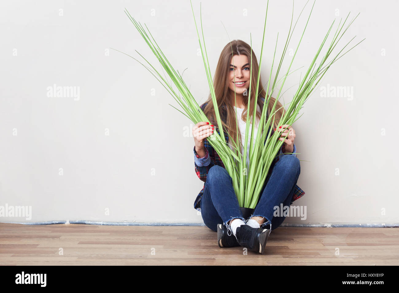 Belle Jeune femme tenant grande plante verte assis contre le mur. Banque D'Images