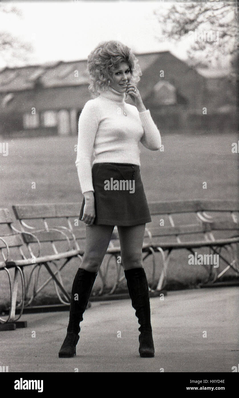 Années 1960, historiques, blonde woman posing en extérieur dans une mini jupe noire et des bottes aux genoux. Banque D'Images