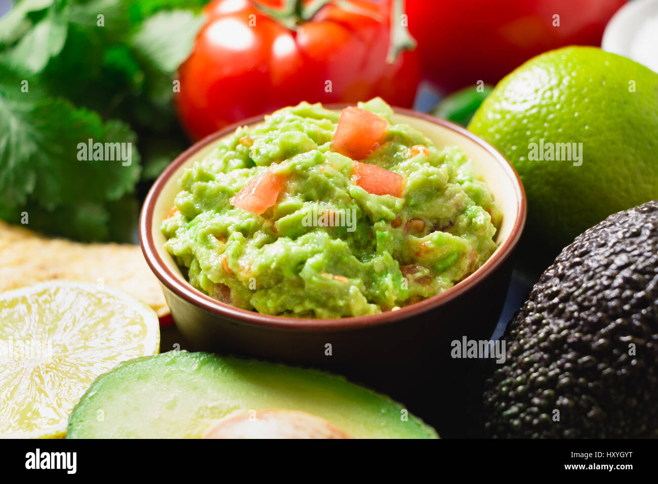 Bol de Guacamole avec des ingrédients et des tortillas sur une table en bois peint en bleu. Banque D'Images