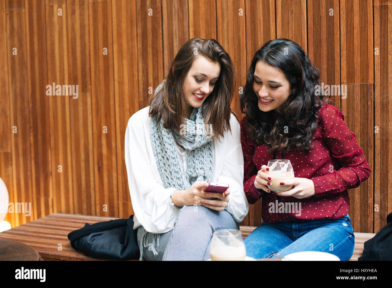 Deux belles jeunes femmes en utilisant un téléphone mobile tout en ayant un café dans un café Banque D'Images